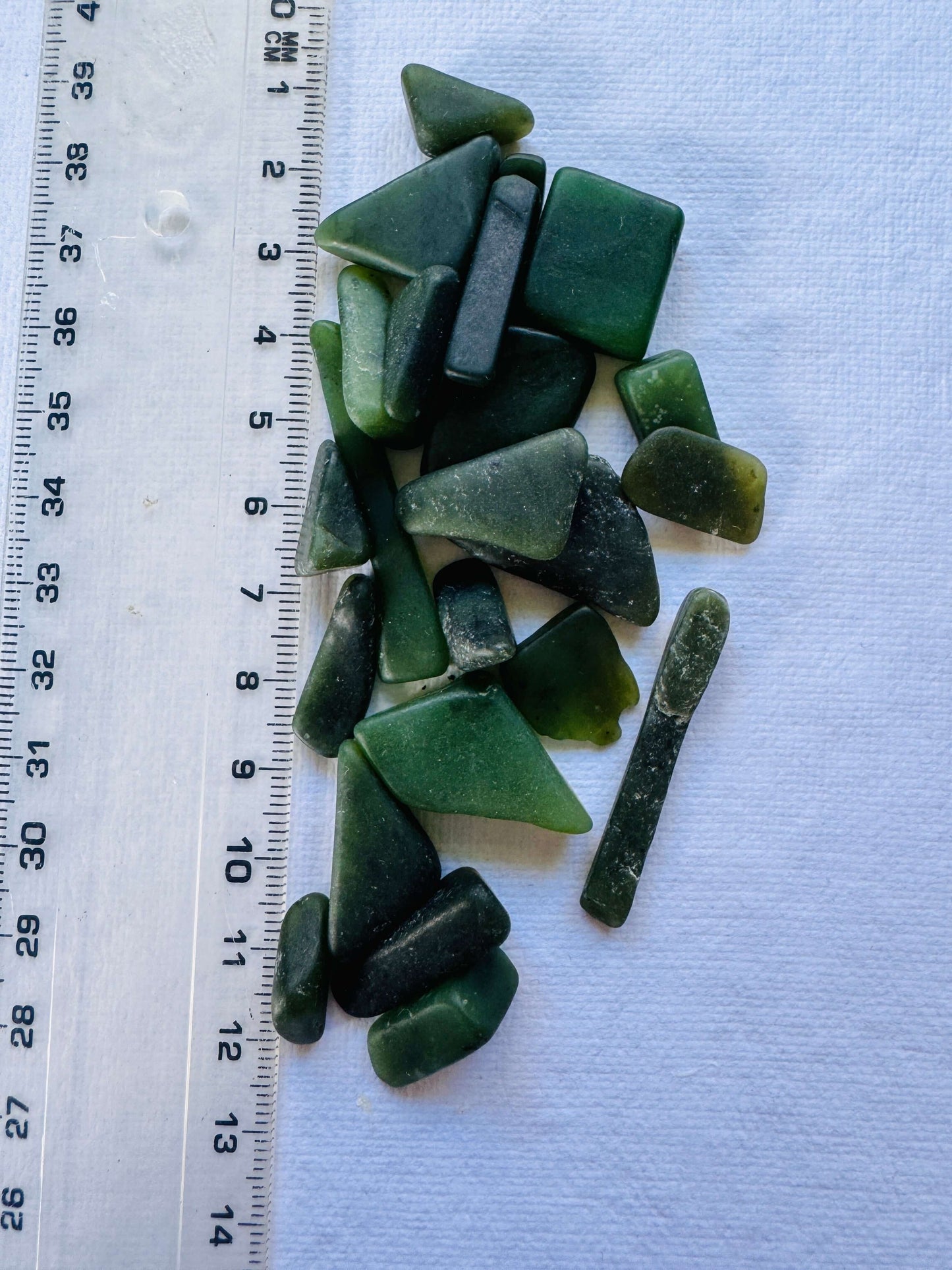 NZ greenstone pounamu semi-polished off-cuts in various natural shapes and sizes on white fabric.