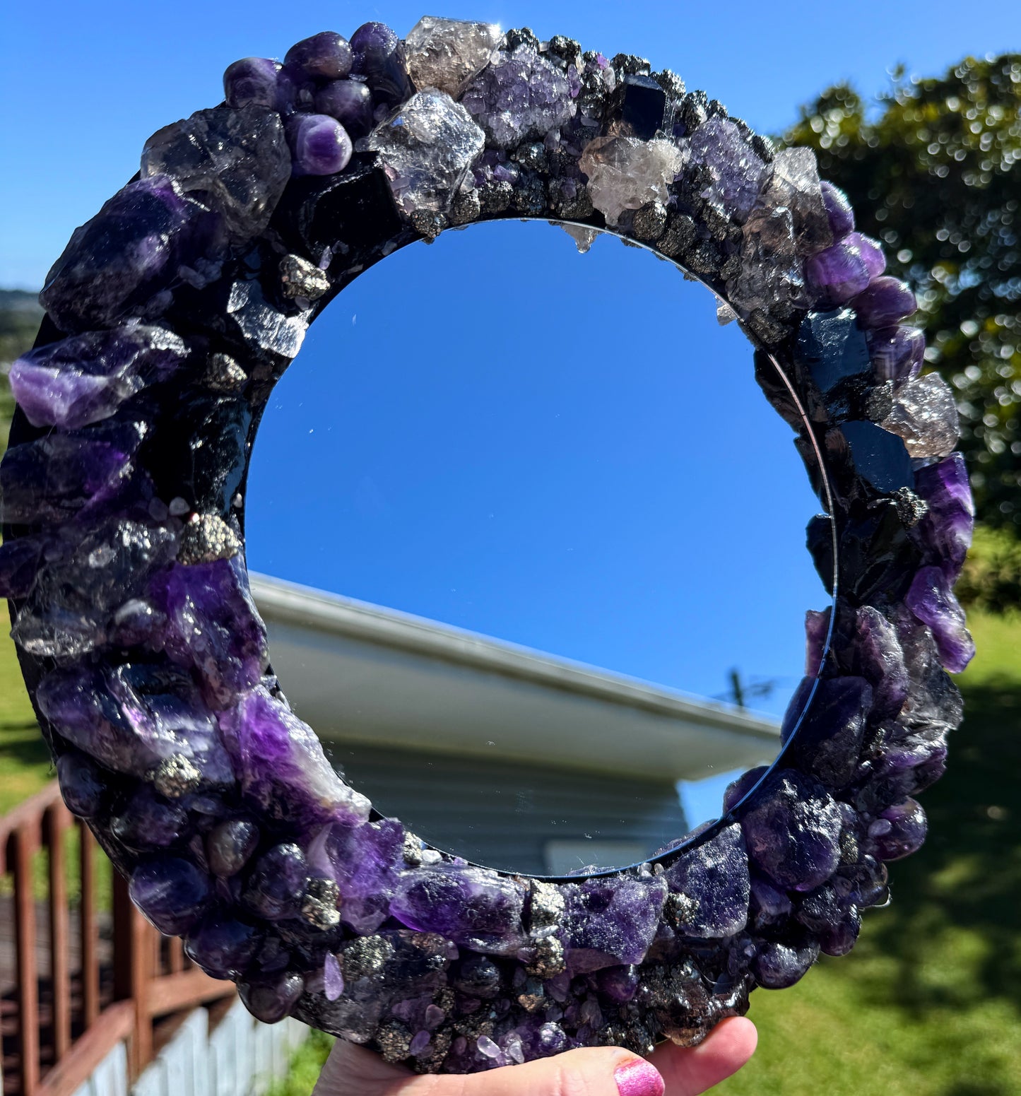 Midnight Magic Crystal Mirror 28cm with amethyst, obsidian, smoky quartz, and pyrite frame reflecting blue sky.