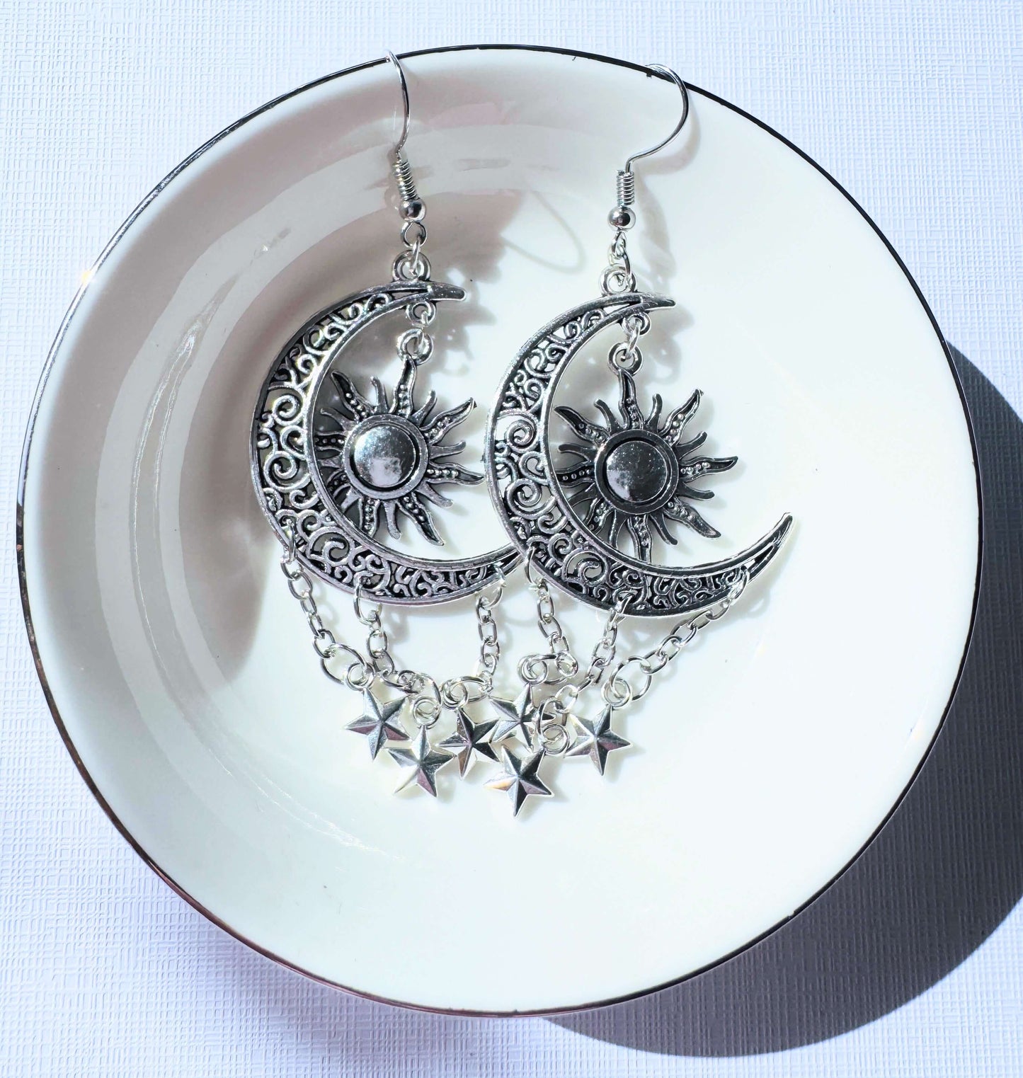 Silver Sun Moon and Stars Earrings with celestial charms on a white dish.