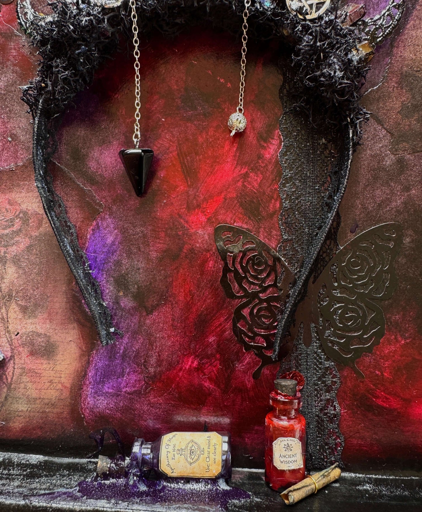 Blood Moon Crown shadow box featuring intricate details, crystals, charms, and pendulum against a vibrant textured background.