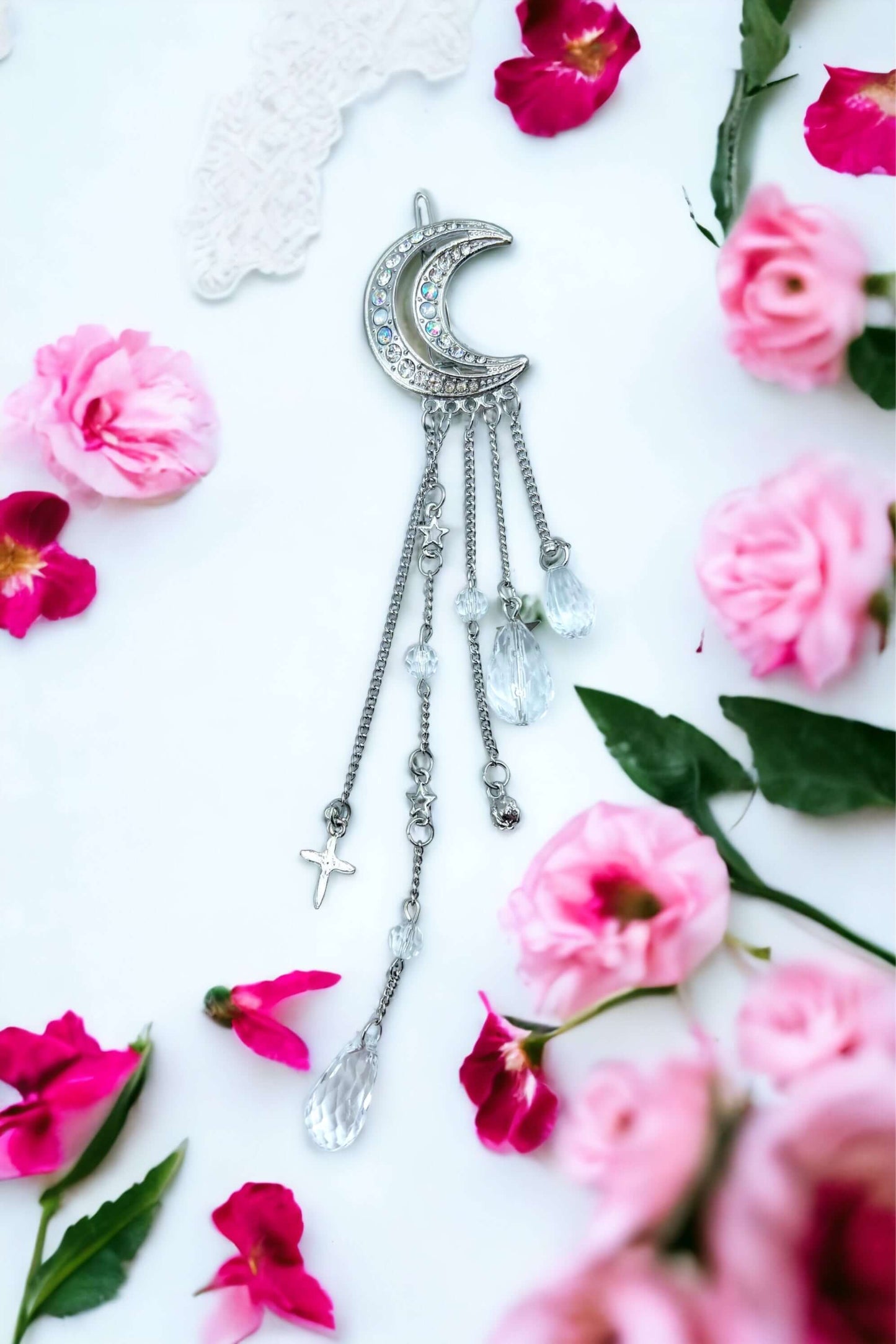 Silver crescent moon hair clip on white surface with scattered petals.