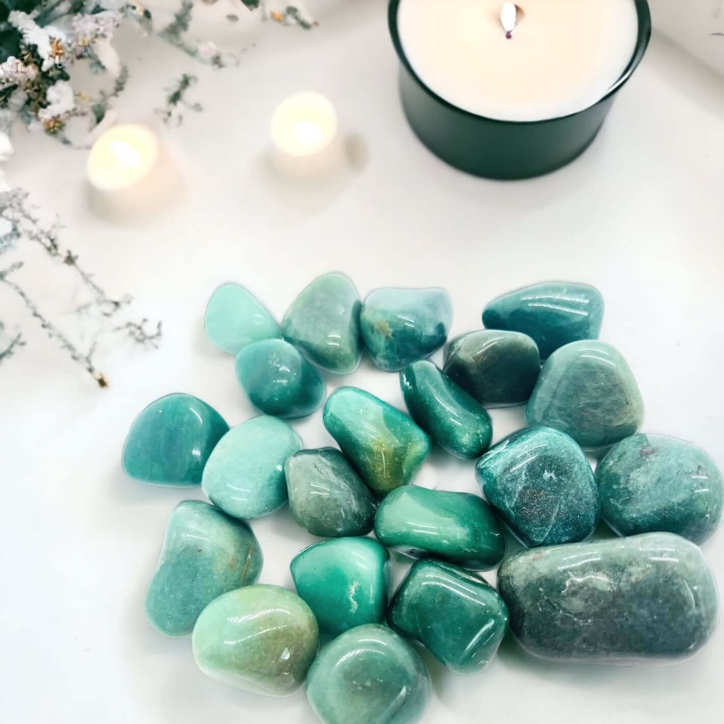 Green aventurine polished stones on a white background with candles.