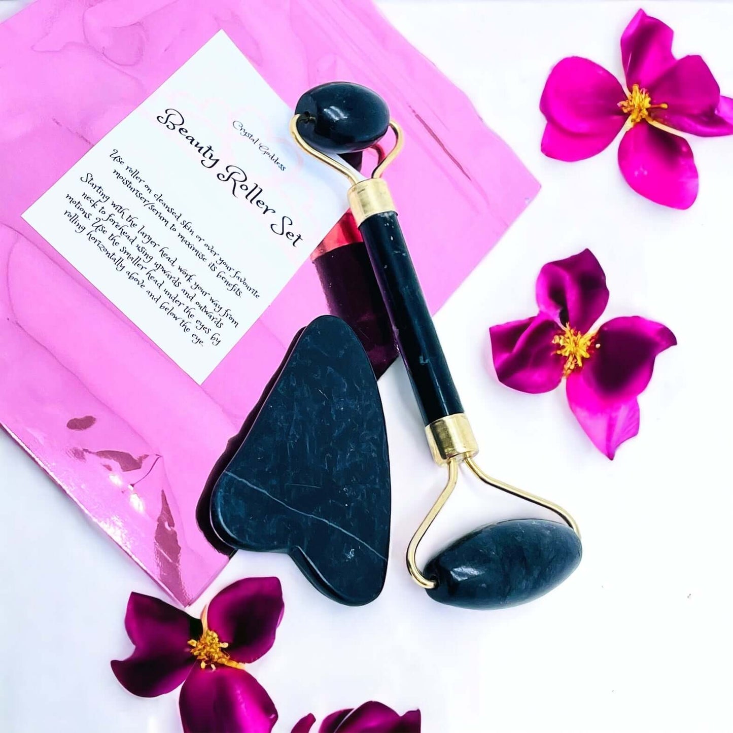 Black Stone gua sha and face roller set on white surface with petals.
