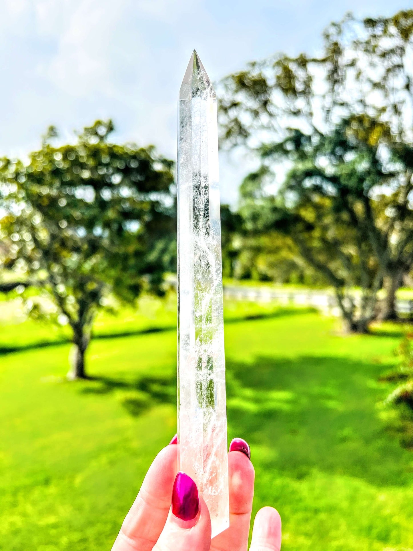 Clear quartz polished point held in hand with farm land in background.