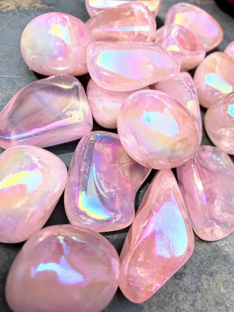Iridescent pink tumbled crystals collection laid out on a textured surface.