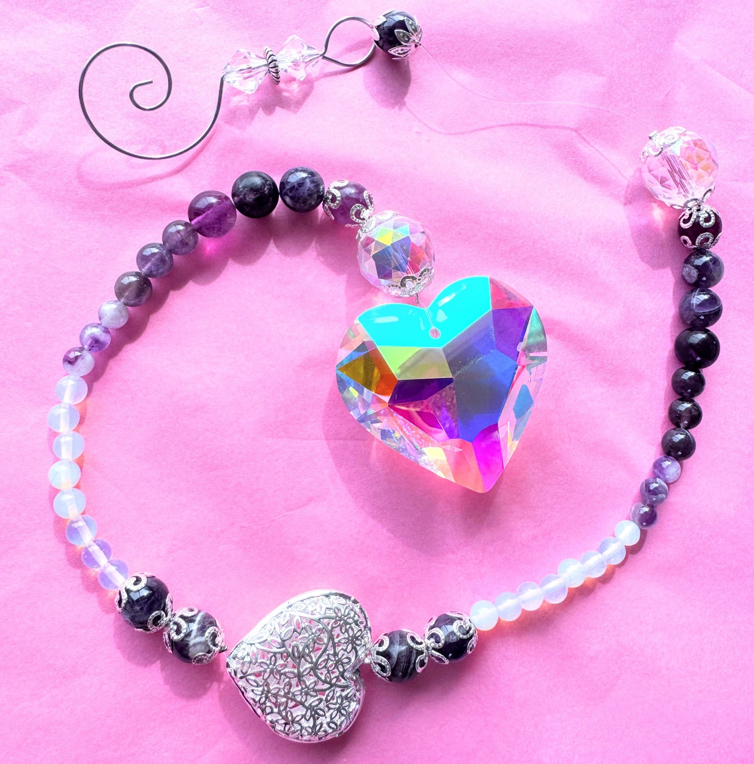 Colorful heart-shaped sun catchers with beaded design on a pink background, capturing and reflecting sunlight for a magical effect.
