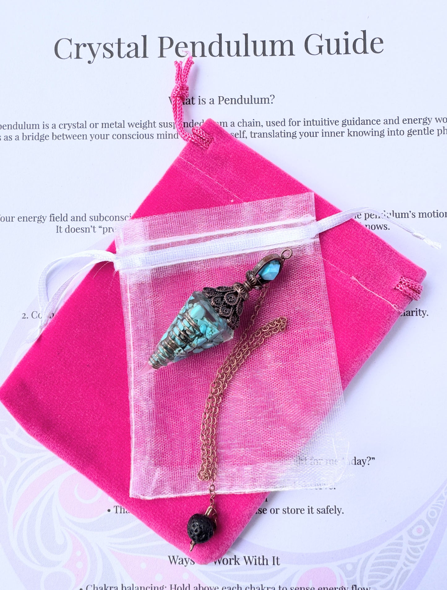 crystal pendulum with bronze chain and bead, displayed with pink pouch and printed pendulum guide