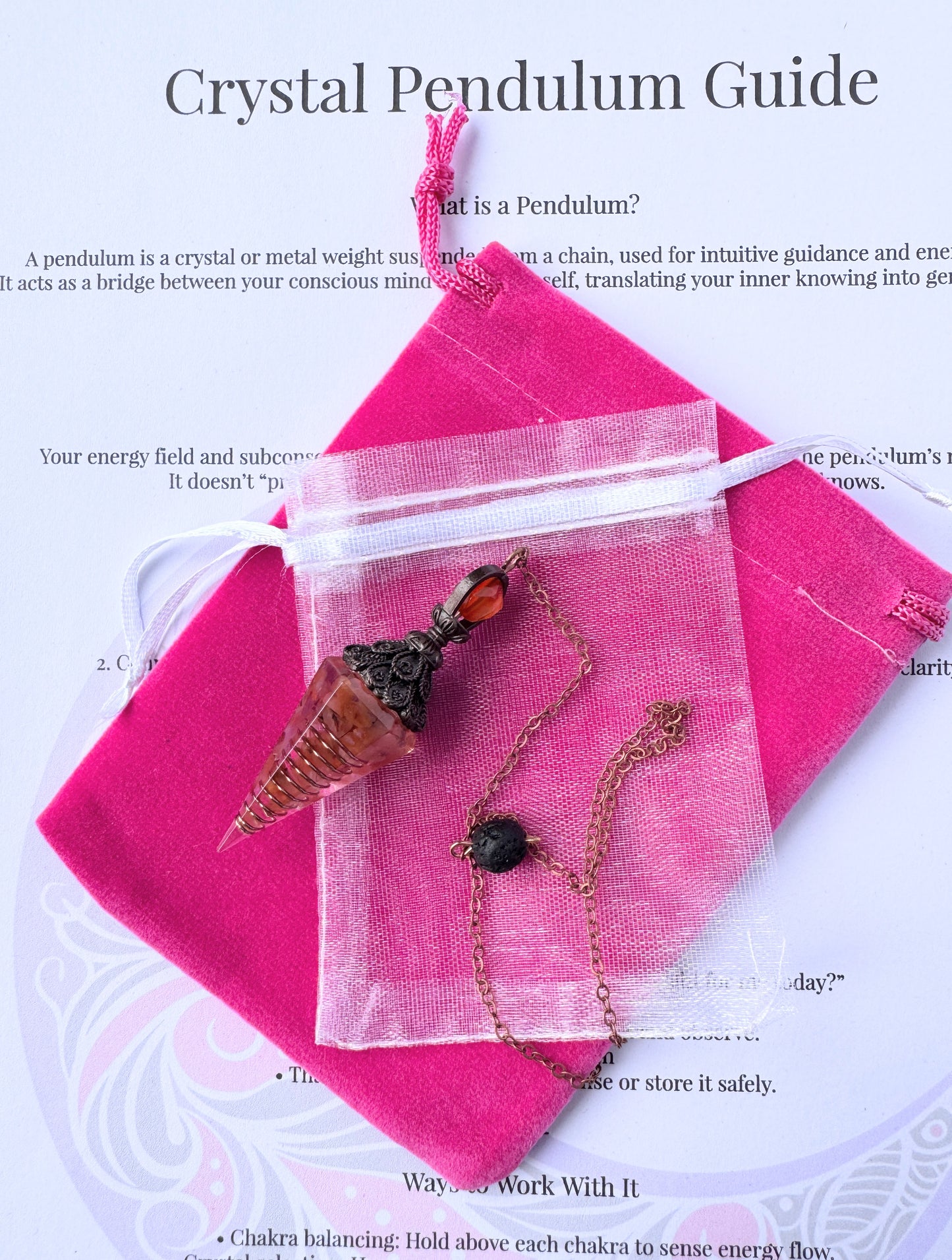  crystal pendulum with bronze chain and bead, displayed with pink pouch and printed pendulum guide