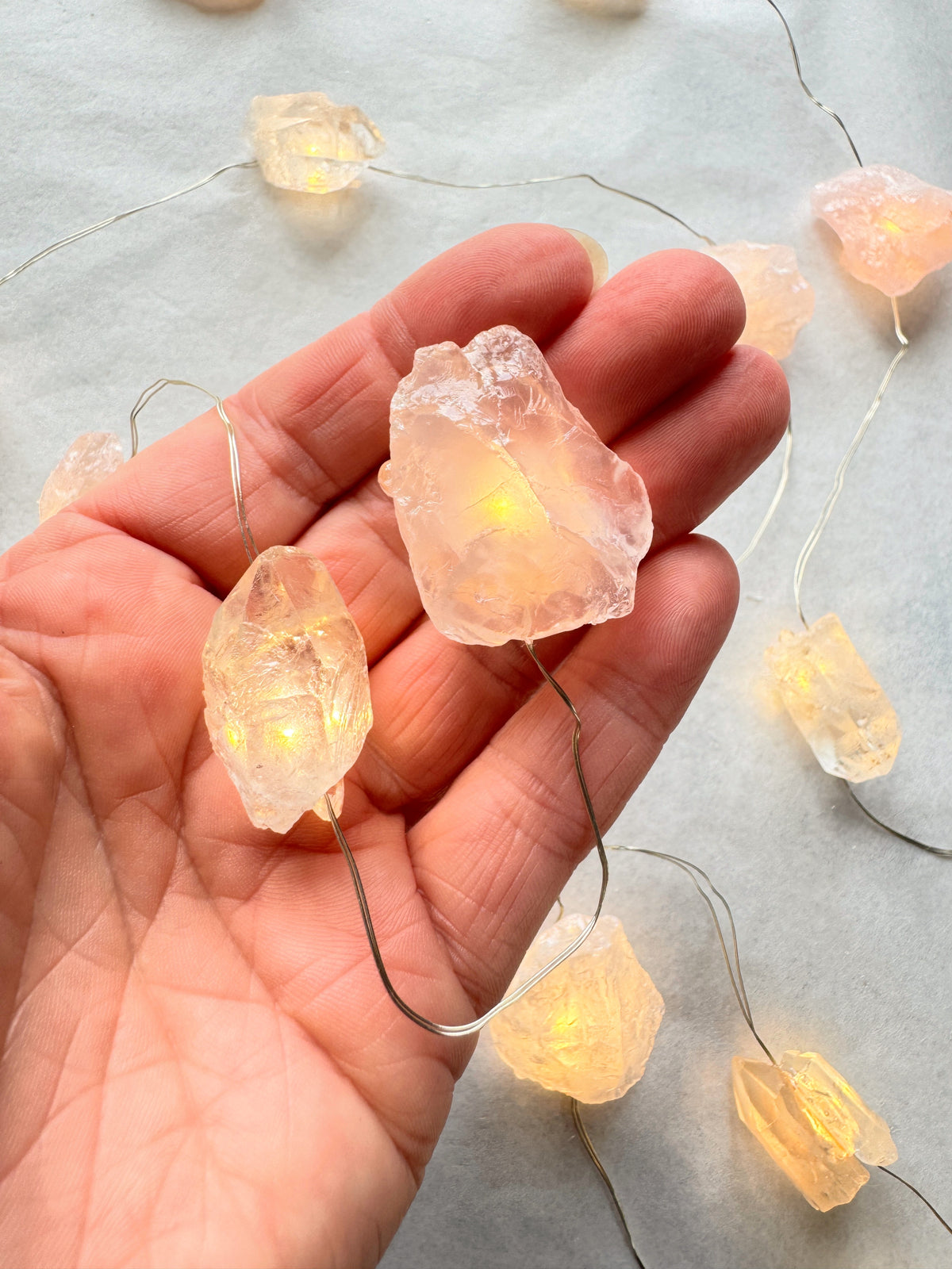 Crystal fairy lights in a hand, featuring rose quartz and clear quartz with warm light, enhancing your space's energy.
