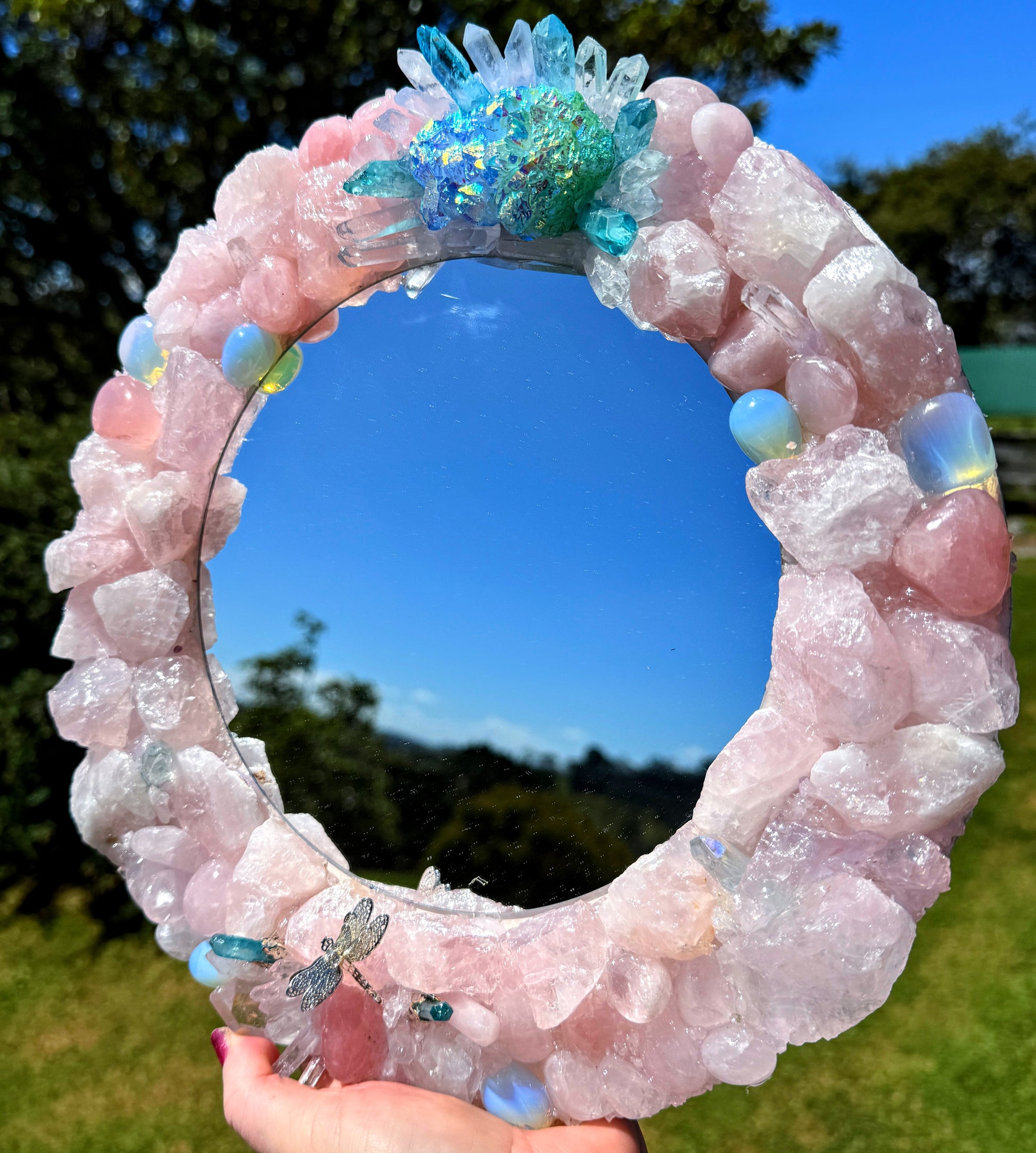 Mermaids Magic Crystal Mirror 28cm with rose quartz, clear quartz, opalite, and blue-green aura quartz cluster in sunlight.