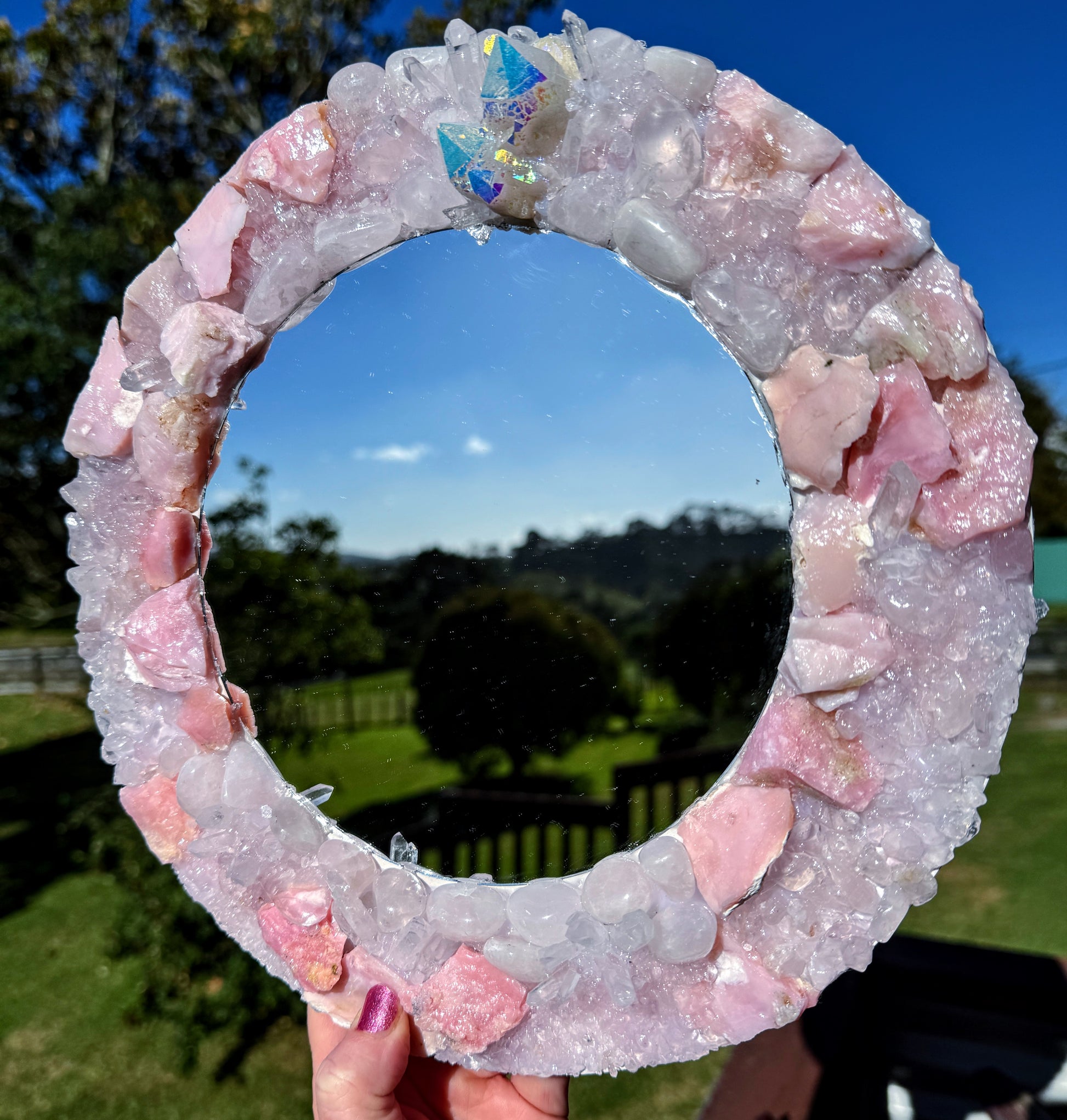 Angel Aura Crystal Mirror 28cm featuring Pink Opal, Rose Quartz, and Clear Quartz against a natural landscape background.