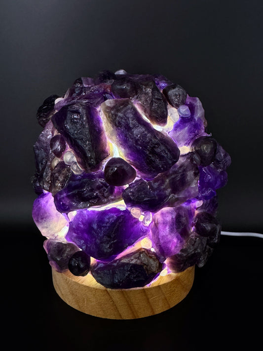 Amethyst Dome Lamp with 10cm base, featuring dark purple amethyst crystals, glowing beautifully when illuminated on a wooden stand.