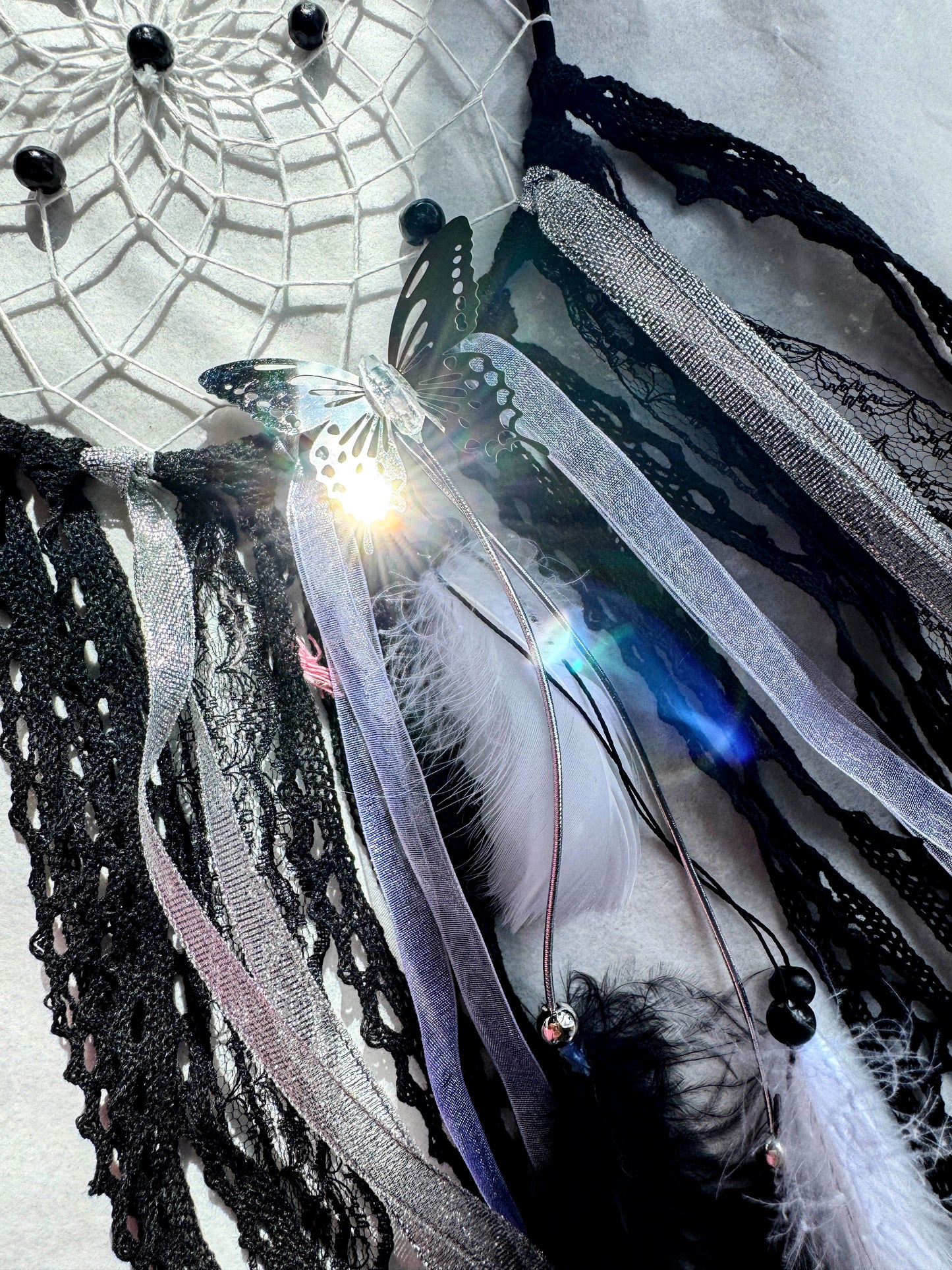 Black dream catcher featuring lace, ribbons, feathers, and a butterfly accent, embodying a grounded energy.