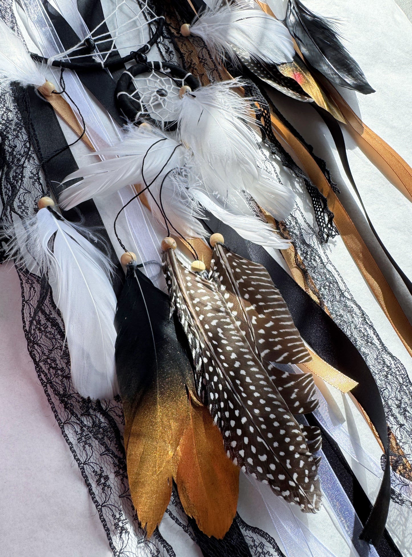 Close-up of a black large dream catcher featuring feathers, lace, and layered ribbons in earthy tones.