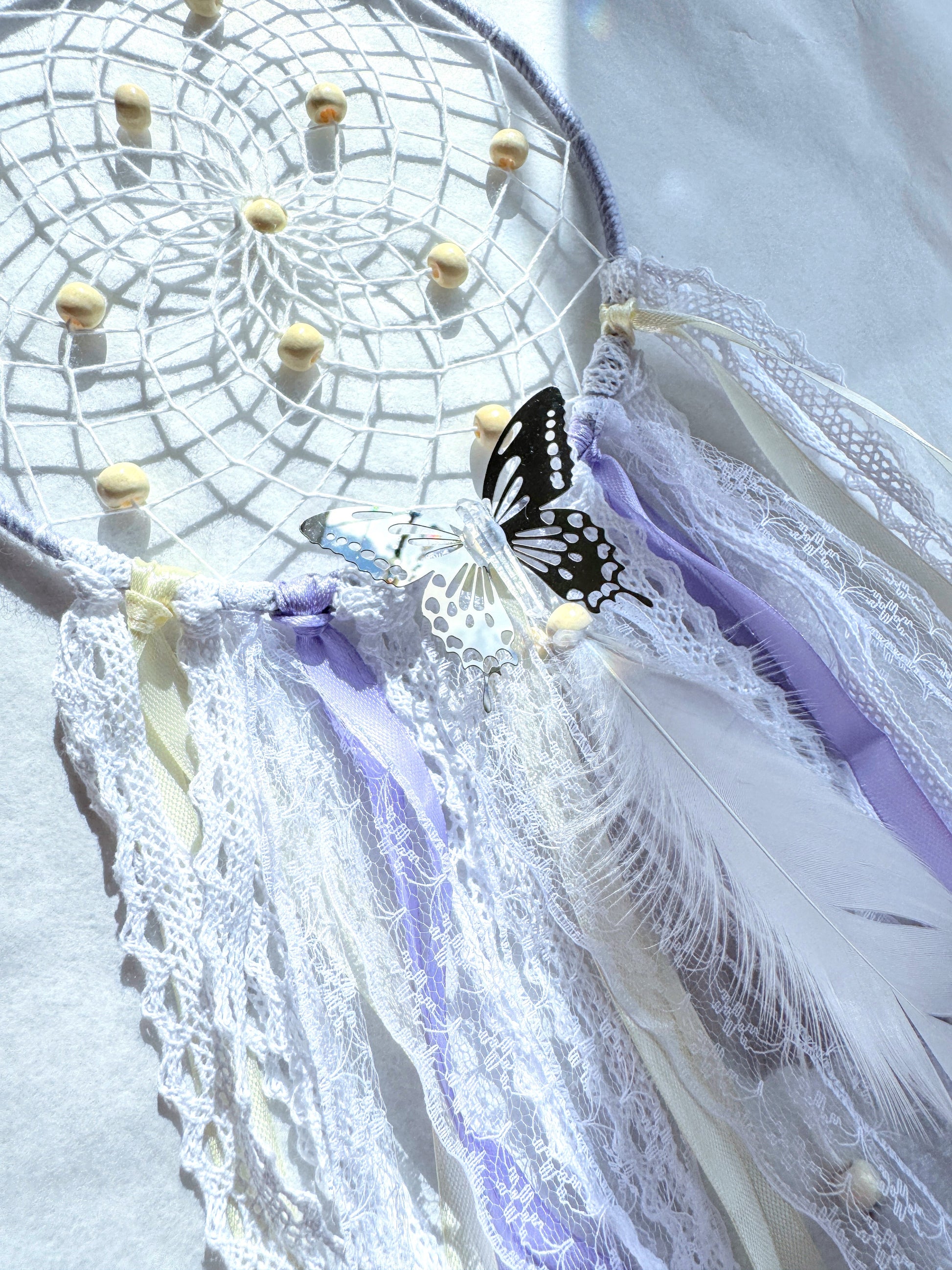 Lavender dream catcher with delicate lace, ribbons, feathers, and a butterfly for a calming space.
