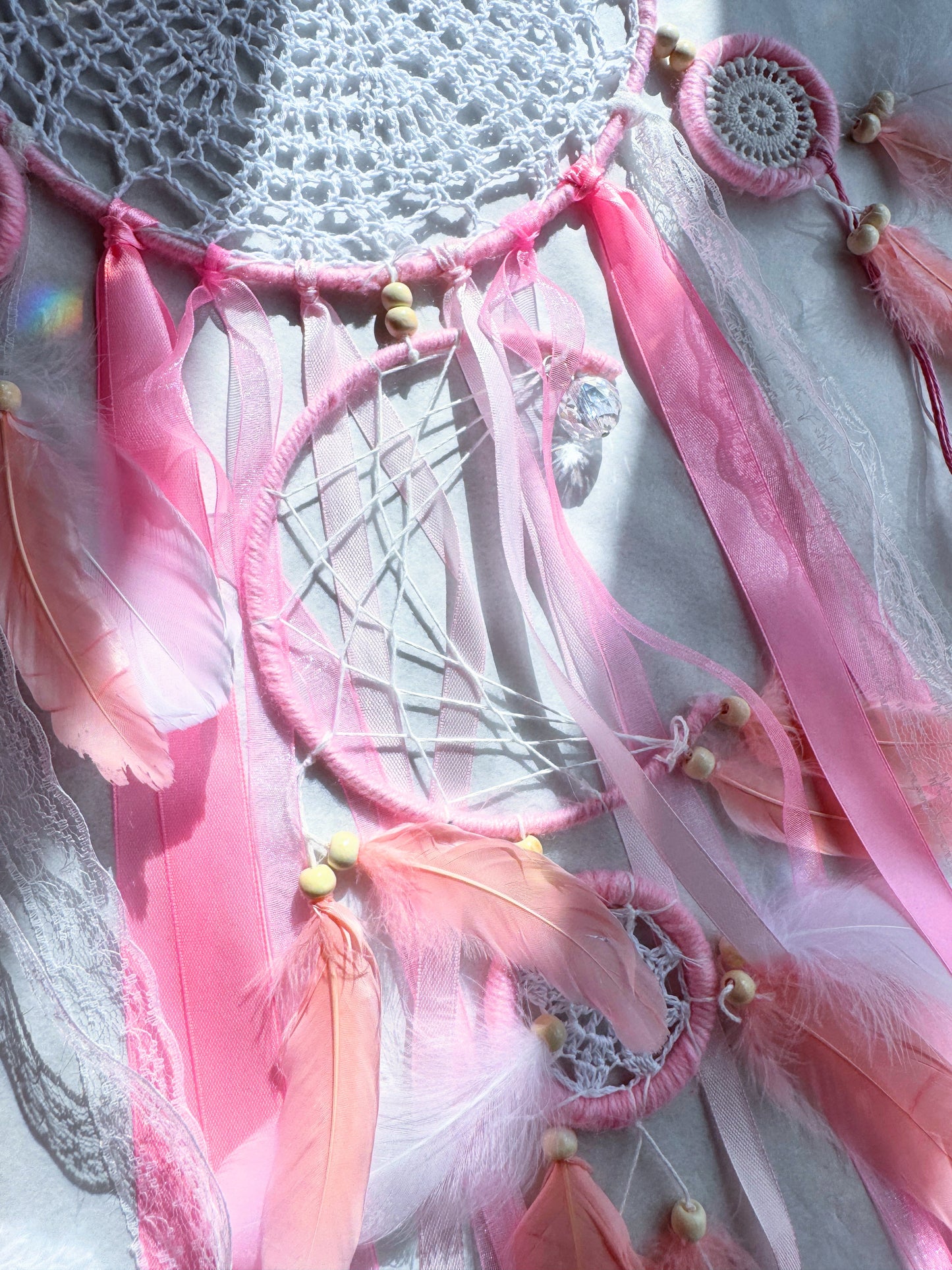 Pink large dream catcher featuring delicate web, flowing ribbons, and feather accents in pastel tones.