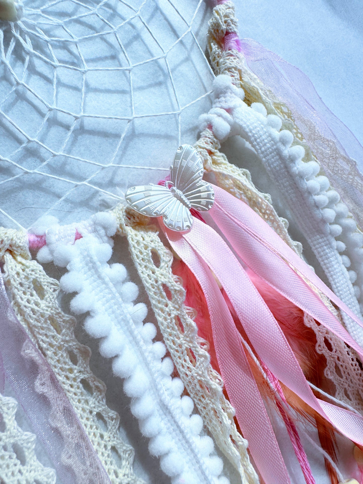 Close-up of a pink dream catcher with lace, ribbons, and a butterfly accent, adding softness and warmth to any decor.