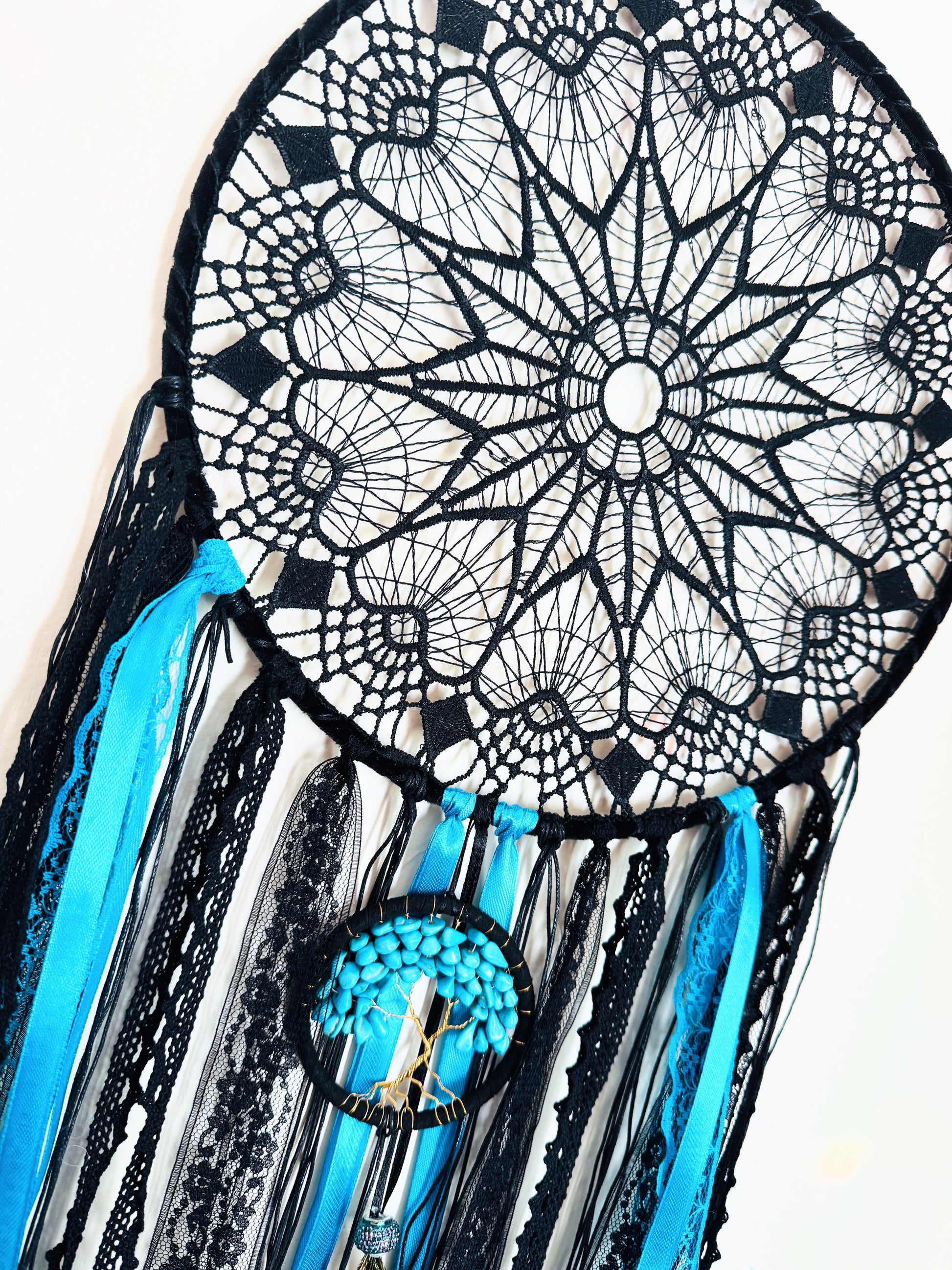 Large turquoise and black dream catcher with lace web, ribbons, and feather details.