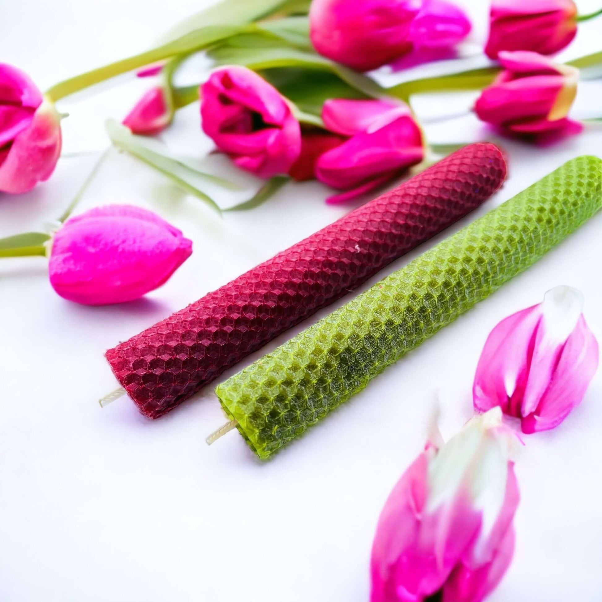 red and green hand rolled beeswax candles surounded by flowers.