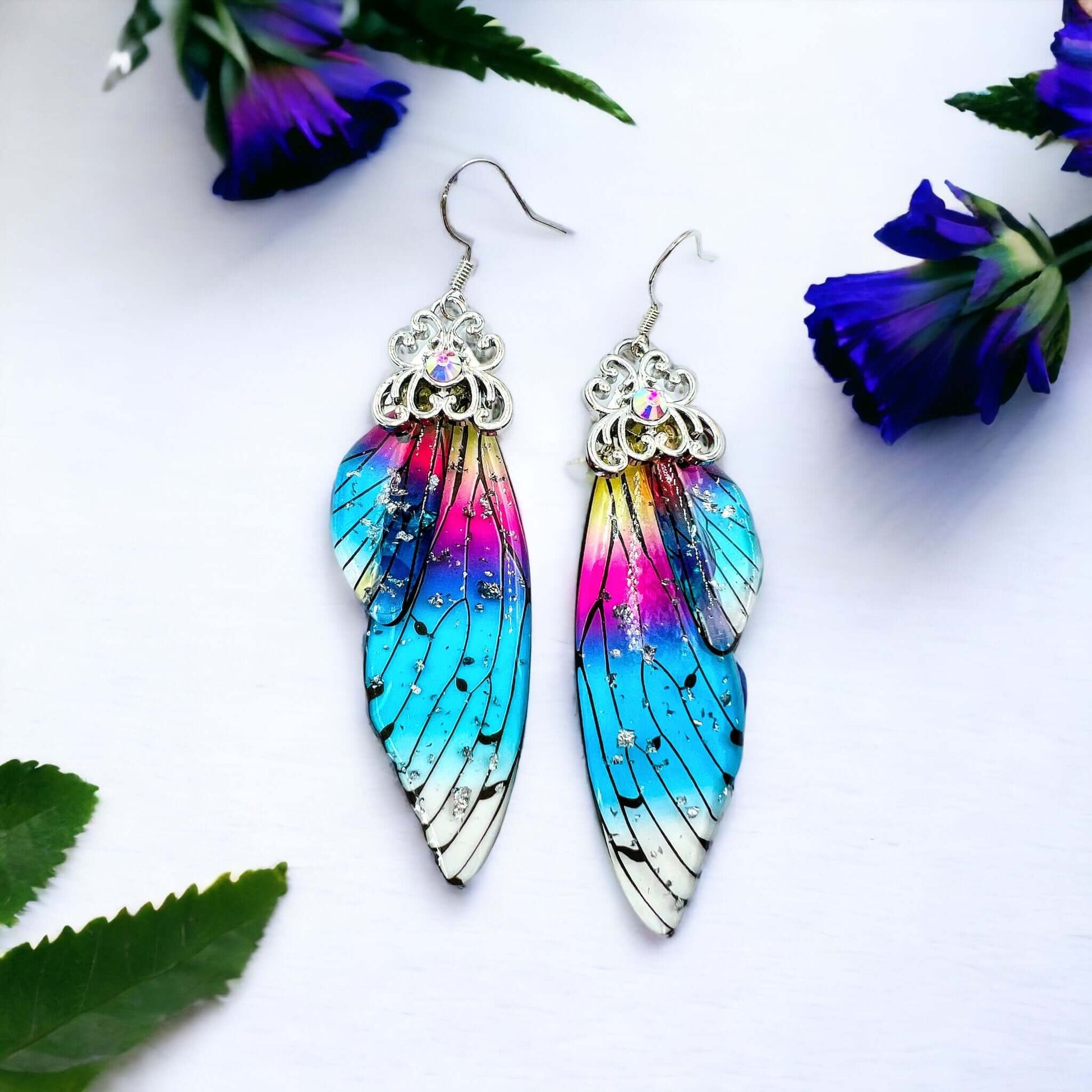 Fairy wing earrings with petals scattered on a white surface.