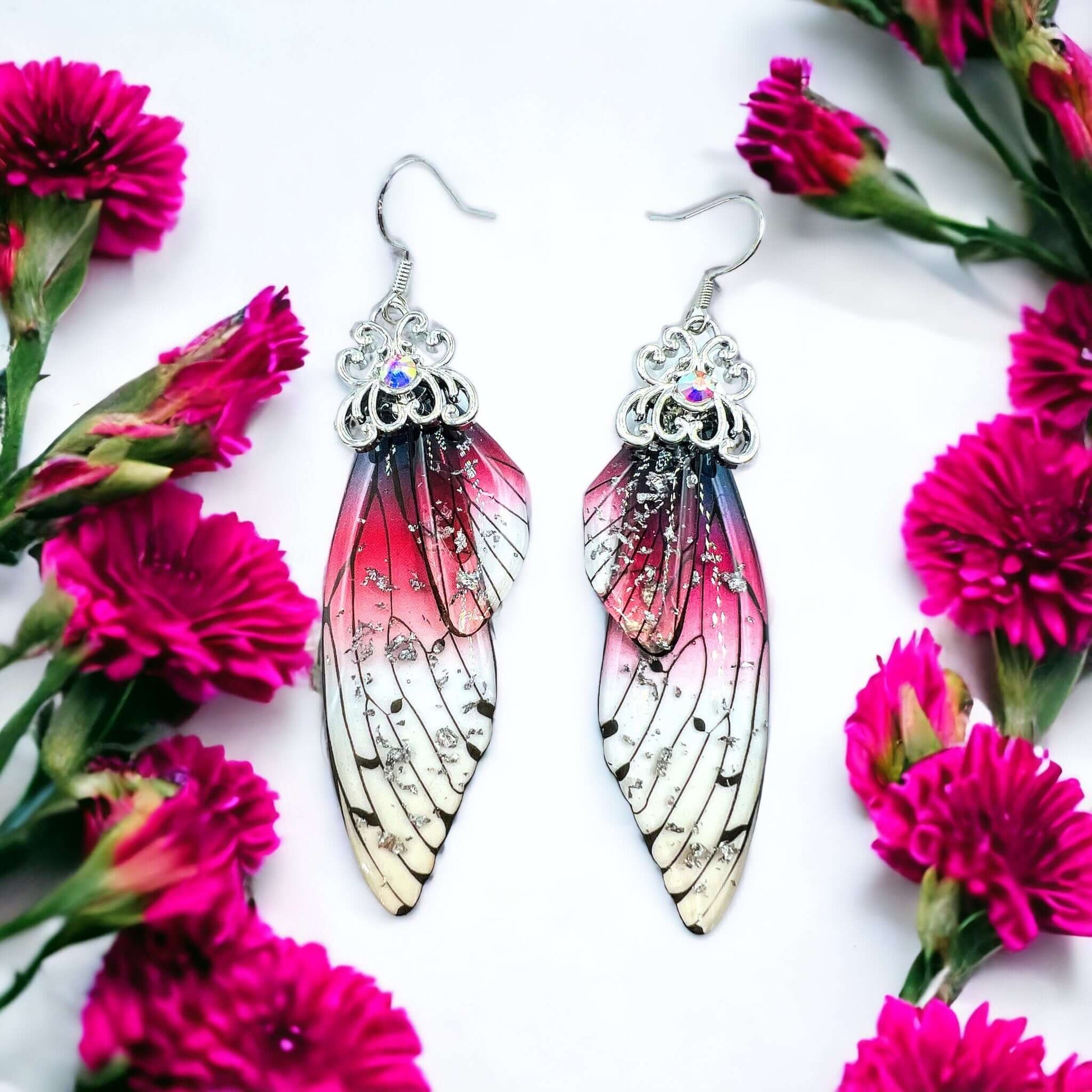 Fairy wing earrings with petals scattered on a white surface.