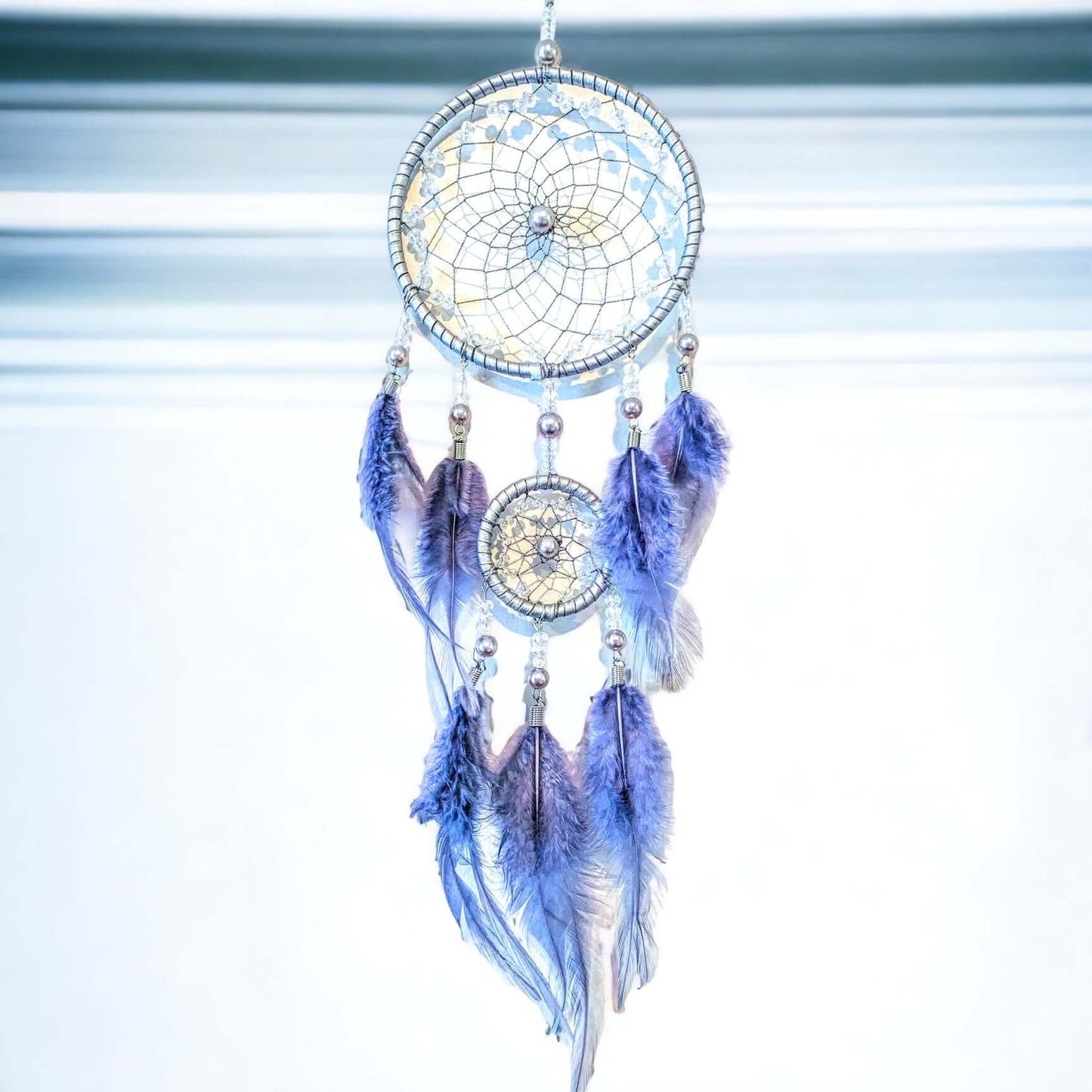 Blue and silver dream catcher with beads and blue feathers on white wall