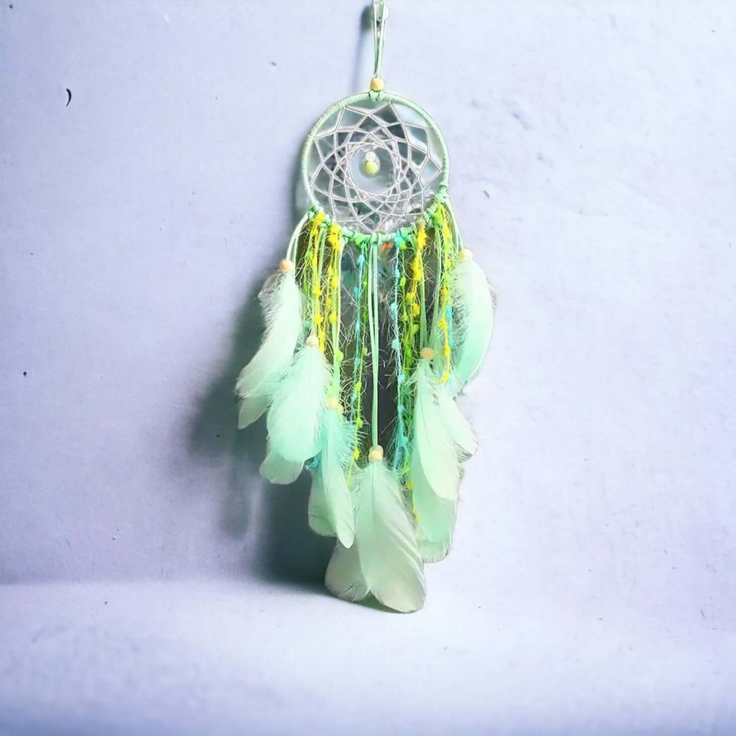 Green and yellow feather dream catcher on white wall