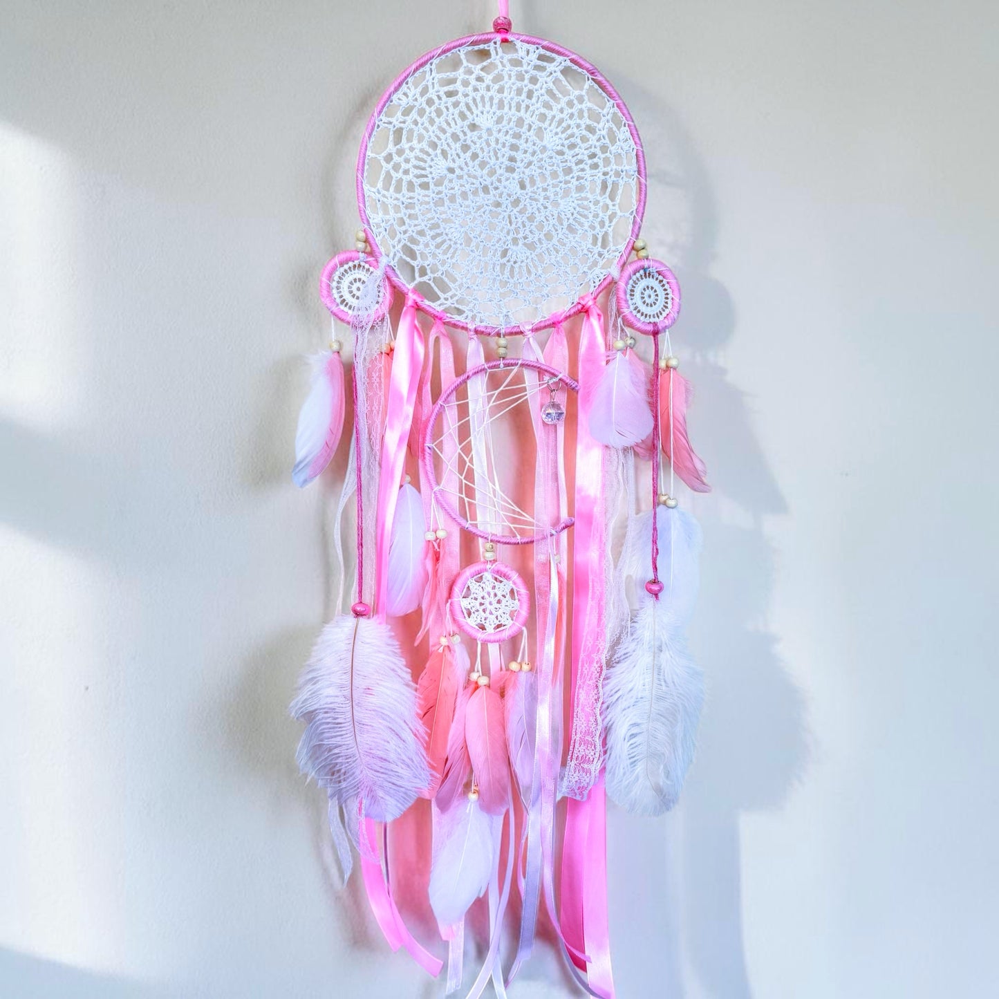 Pink large dream catcher with delicate woven web, ribbons, and feather accents in soft pastel tones.