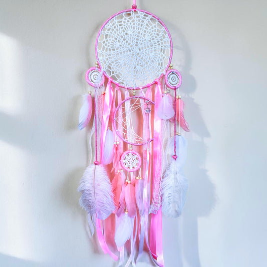 Pink large dream catcher with delicate woven web, ribbons, and feather accents in soft pastel tones.