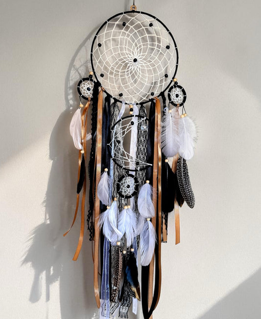 Black large dream catcher featuring a woven web, layered ribbons, and feathers in black, white, and earthy tones.