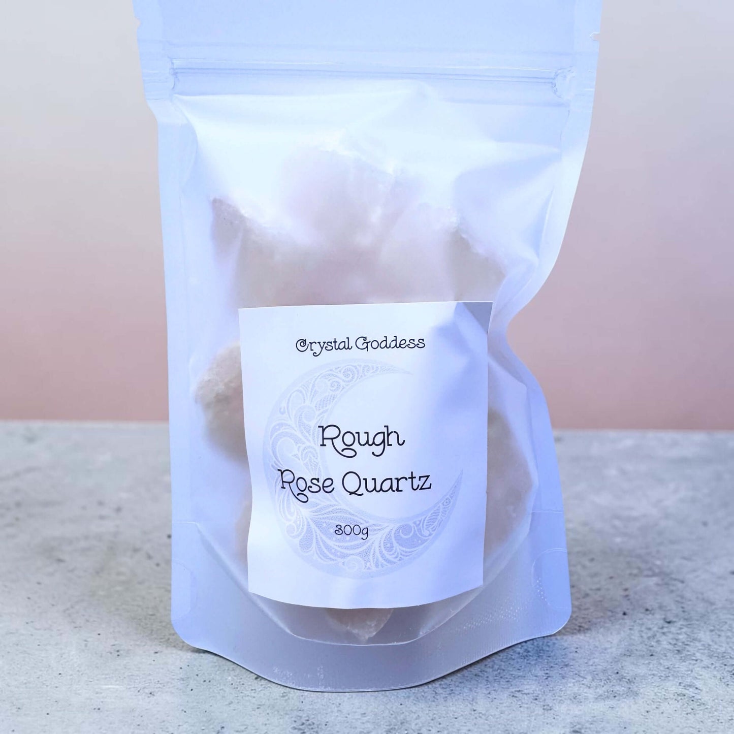 Rough Rose Quartz stones 300g in a clear bag with a white label, showcasing soft pink natural crystals.