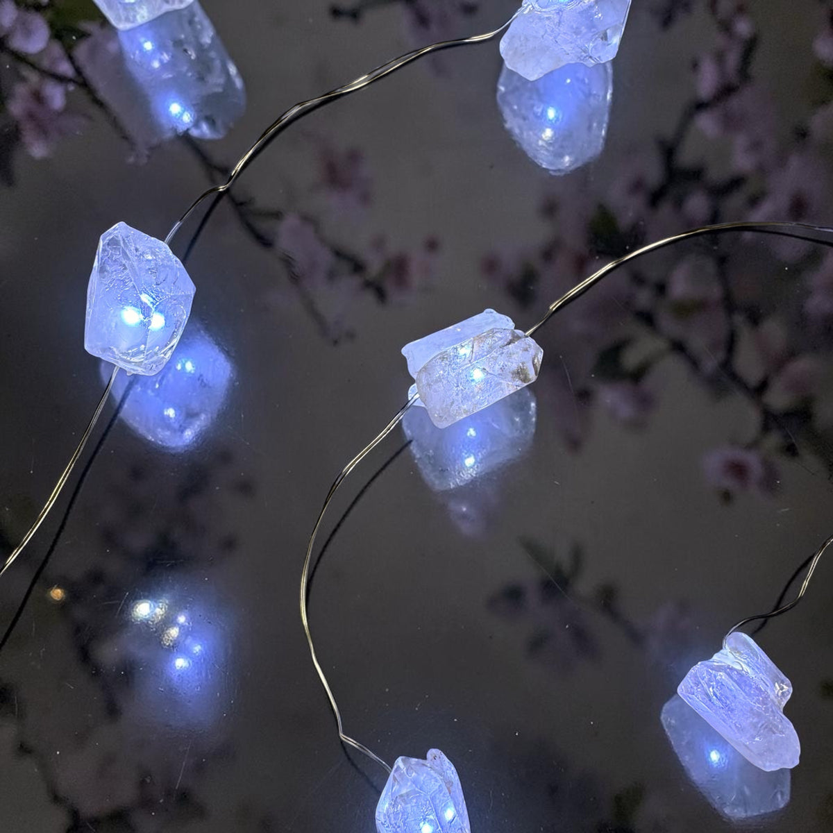Crystal fairy lights illuminating clear quartz crystals with a soft glow on a reflective surface.