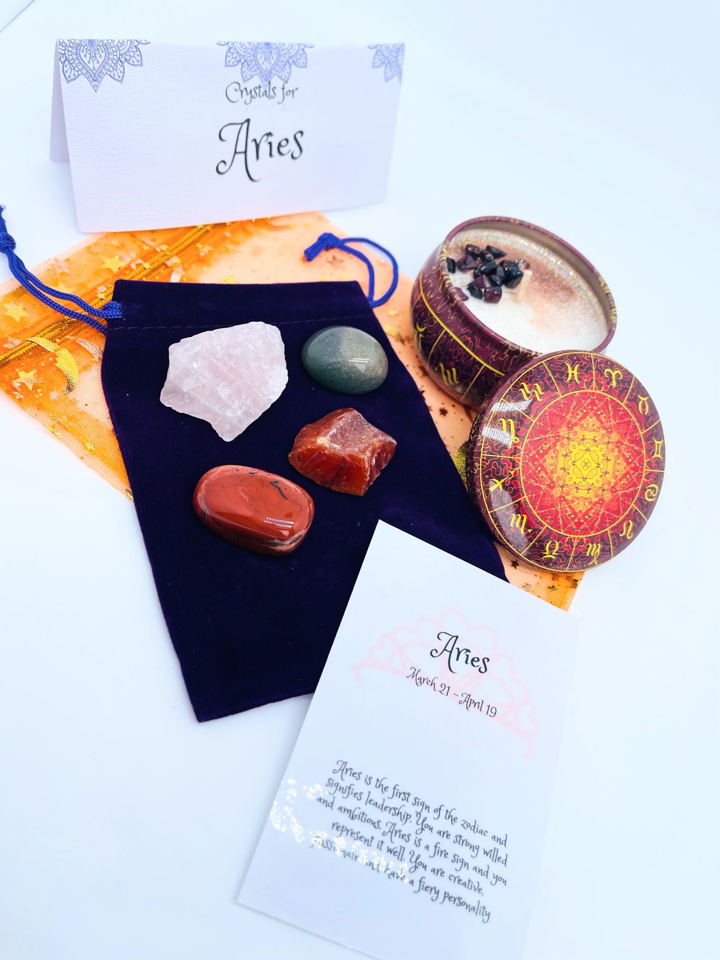 Aries zodiac candle gift set with candle and four crystals for this sign sitting on a velvet bag.